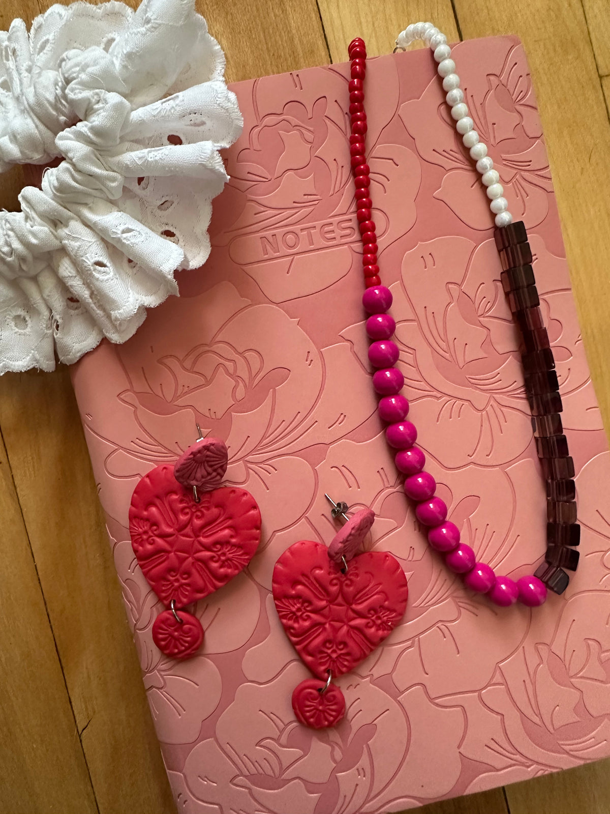 Collier Grenadine posé sur carnet rose avec boucles d'oreilles cœur rouges