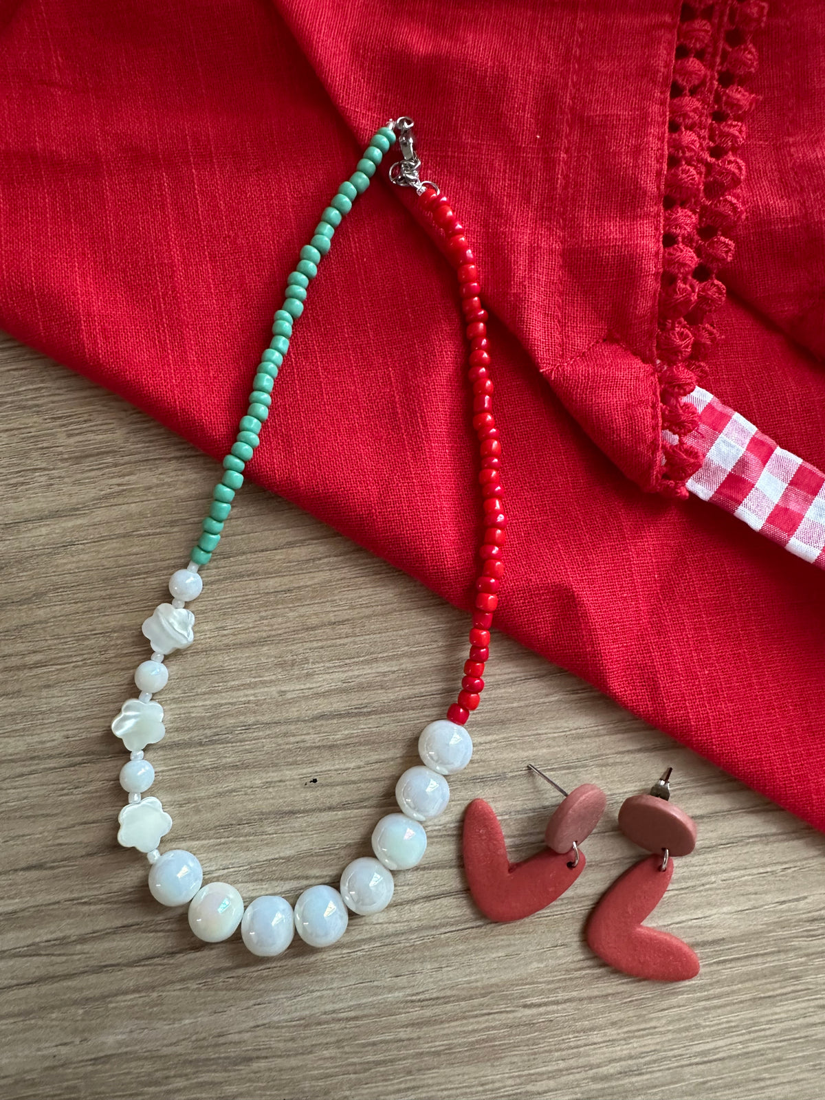 Collier Tropicana posé sur tissu rouge avec boucles d'oreilles cœur terracotta