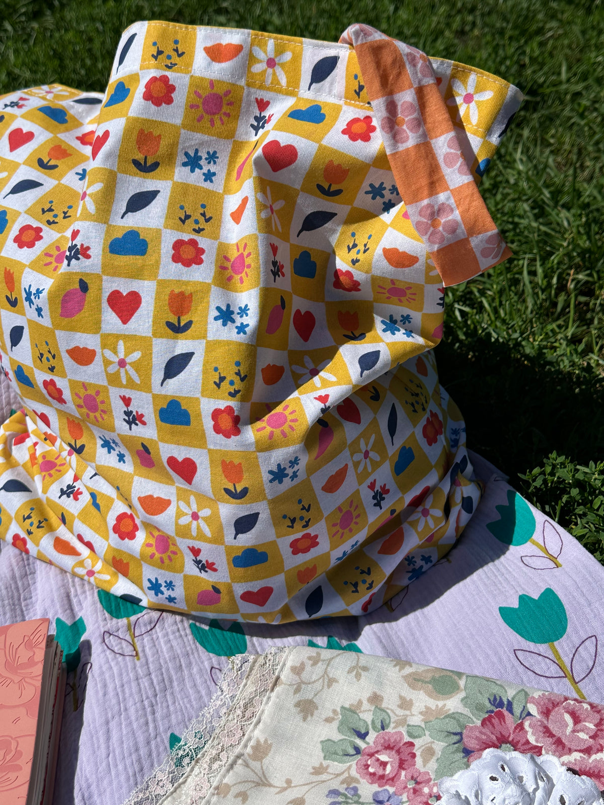 Sac Lisette damier fleuri posé sur une nappe lilas, vue de côté